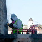 A worker wearing protective gear cleans the exterior limestone of Franklin Hall