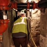 A worker in a yellow vest ducks down in a narrow space