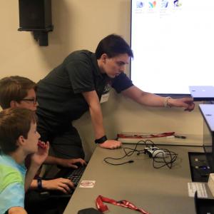 A camp staffer points to a computer screen while two campers look on