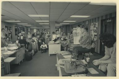 A black and white photo of students in a semi-circle, looking toward a student holding up a copy of the IDS.