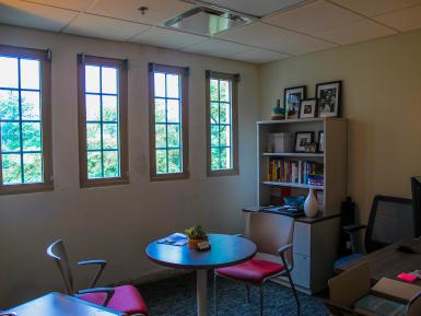 An advising office in Ernie Pyle Hall, with a tall bookshelf, three narrow windows and a desk with two seats