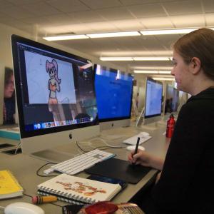 A student using a drawing tablet, sketching a character with a pink ponytail