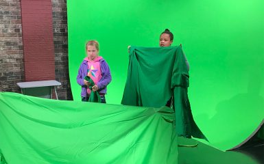 Two young girls stand before a green screen