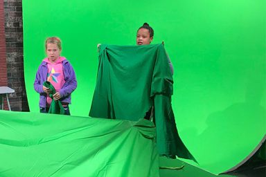 Two young girls stand before a green screen