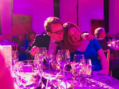 A man and woman sitting at a dinner table embrace