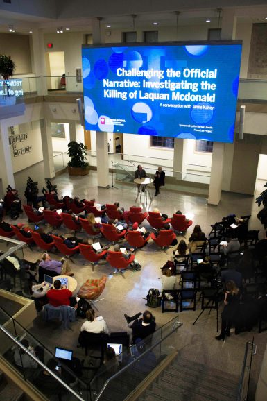 Audience members watching two men talk under a screen that says "Challenging the Official Narrative: Investigating the Killing of Laquan McDonald"