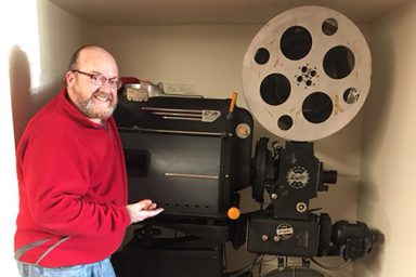 IUPUI alumnus and Chinese film actor James Lee Guy stands next to the 1937 Peerless/Simplex model E-7 projector he donated to The Media School.