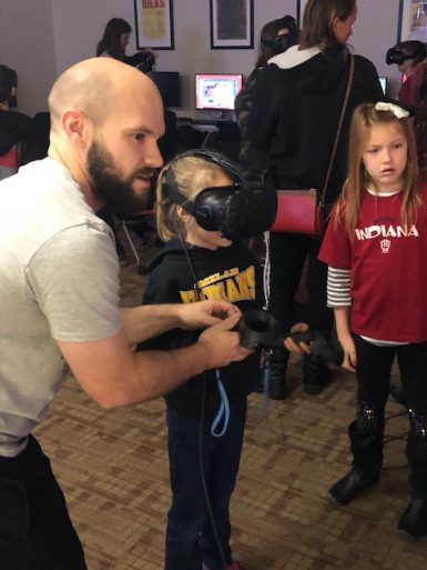Lecturer Rush Swope helps a young Science Fest guest carve a virtual pumpkin using virtual reality equipment while another participant looks on