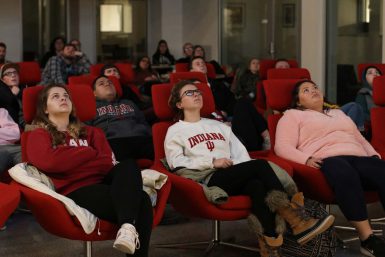 Students sitting in red chairs, looking up.