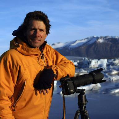 James Balog standing with a camera and tripod in front of a mountain in Iceland