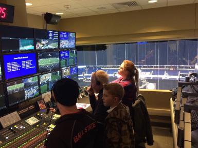 Four people watching screens in a broadcast control room at Lucas Oil Stadium