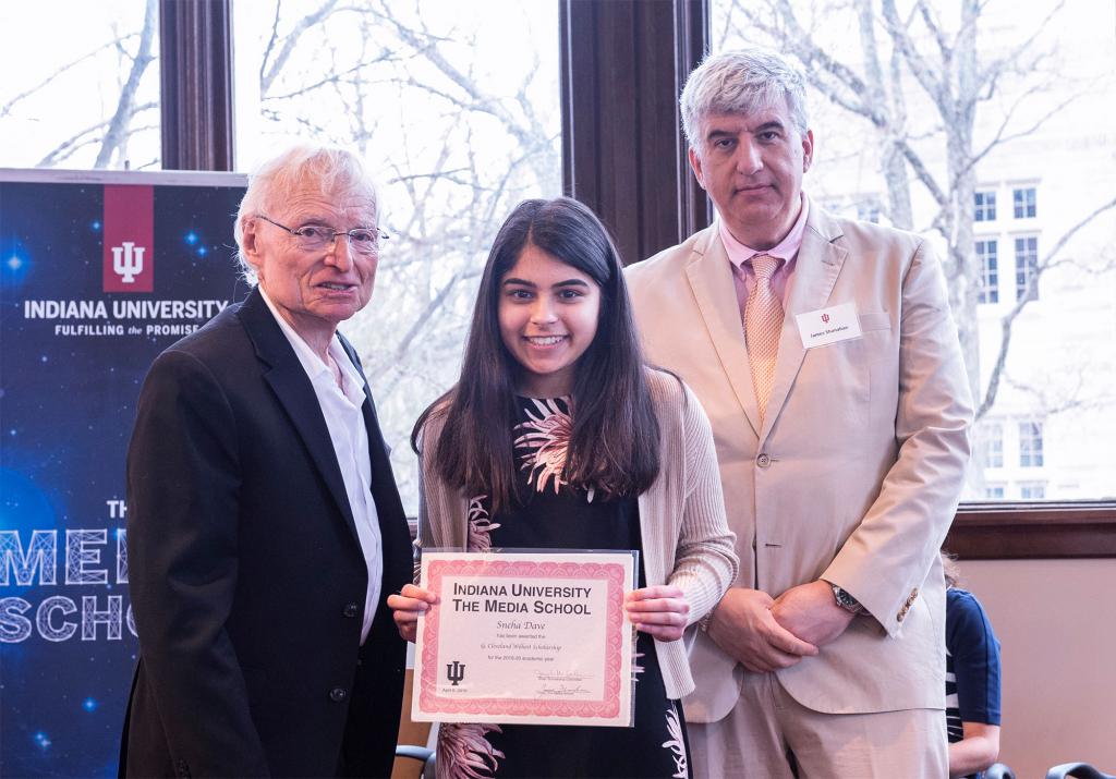 Cleve Wilhoit, Sneha Dave and Jim Shanahan pose together ona stage. Dave holds up a certificate that says "G. Cleveland Wilhoit Scholarship."