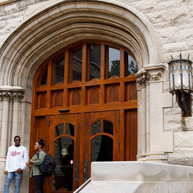 Three people stand on the entrway steps of Franklin Hall.