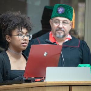 A game design student gives a presentation as professor of practice Mike Sellers watches at the game design graduation celebration.