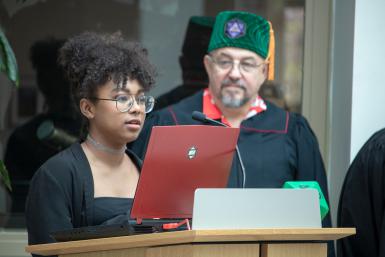 A game design student gives a presentation as professor of practice Mike Sellers watches at the game design graduation celebration.