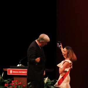 Ying Yang, the last graduate to walk across the stage, stops to talk a selfie with dean Jim Shanahan and the audience.