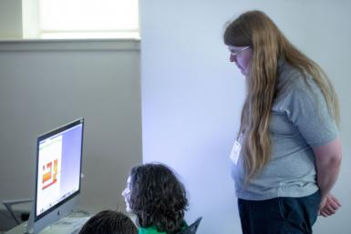 Counselor Avery Cortell watches a student create an illustration on a computer.