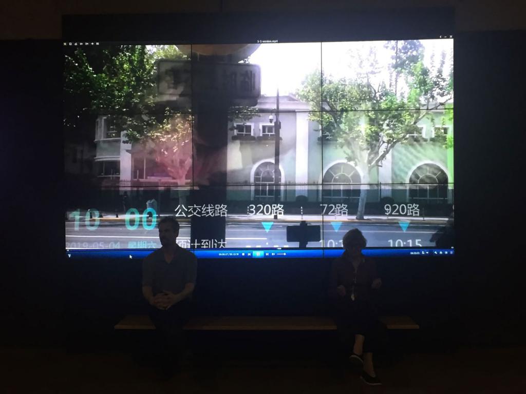 Artist Petra Johnson and Marceau Chenault sit in front of a video screen depicting an empty streetscape.