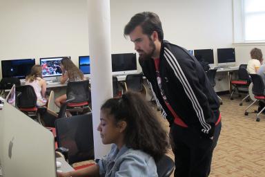 Sam House looks over a student's shoulder as she works on a computer.