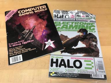 Two magazines. One is Computer Gaming World. The cover says: "LucasArts' X-Wing Fighter. Also in this issue: Global Effect, The Two Towers, Sea Rogues Strategy, Aces of the Pacific Tactics. 100 Games Rated!" The second is Electronic Gaming Monthly. It says "We played HALO. 14-page blowout! Exclusive new screens! Multiplayer Hands-On: New maps and modes. New Vehicles: Mongoose ATV, Brute Ghost. New Weapons: Brute Spiker, Spike grenades, Spartan laser, the new needler. Stuff for everyone from your best bud to the guy who slept with your gal."