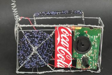 An artistic rendering of a radio made of recycled material: wire, a Coca-Cola can, beads.