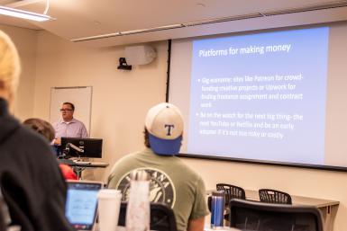 Jay Kinciad teaches a class. His Powerpoint slide says: "Platforms for making money. Gig economy: sites like Patreon for crowd-funding creative projects or Upwork for finding freelance assignment and contract work. Be on the watch for the next big thing -- the next YouTube or Netflix and be an early adopter if it's not too risky or costly."