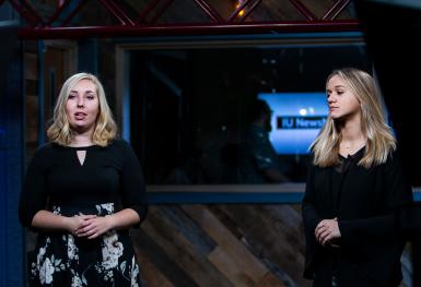 Two people in black talk to a camera.