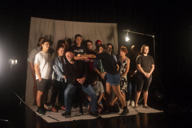 Jonathan Banks poses in a studio with 14 students. Alyssa Woolard pretends to punch him in the face.