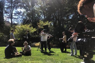 Students film a movie in a grassy area on campus.