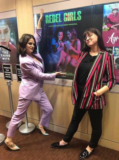 Riley Dismore and Katie Crump pose in front of a "Rebel Girls" poster