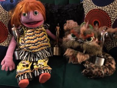 Two puppets hold three Telly awards.