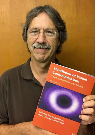 Jim Kelly holding "Handbook of Visual Communication"