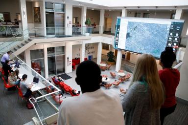 Three students looking at a map on the sreen in the commons