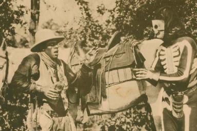 A man wearing a skeleton costume and a man dressed in cowby gear standing in front of a horse.