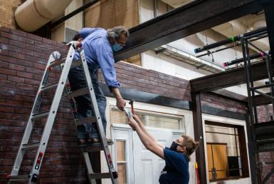 A woman hands an item to Steve Krahnke, who is on a ladder.