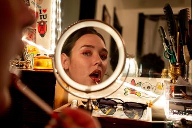 A woman looks in the mirror as she applies makeup.