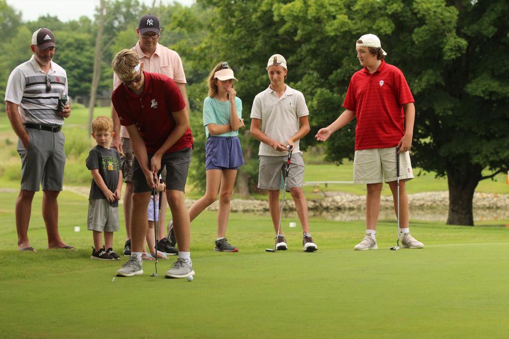 A man putts on a golf course as six people watch.