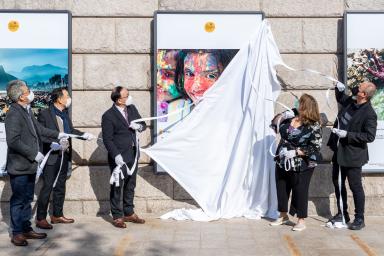 People pull a sheet off a large framed photograph to unveil it.