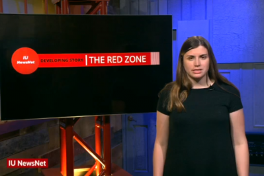 Mary Claire Molloy standing in front of a TV screen that says: IU NewsNet Developing Story: The Red Zone