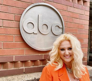A blonde woman stands in front of an abc sign