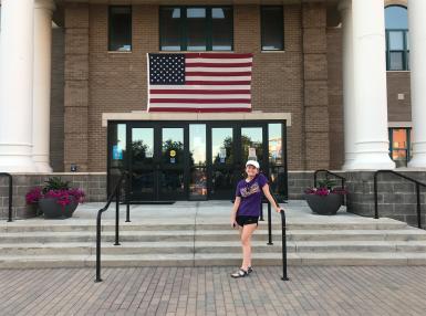 A woman wearing shorts and a T-shirt stands on the stairs outside a Fishers government building.