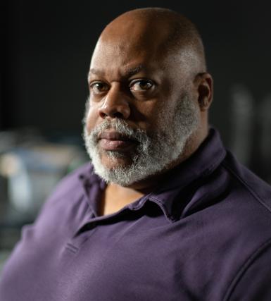 Bear Brown headshot. Bald, Black man with a beard wearing a purple shirt.