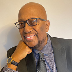 Black man wearing glasses and suit smiles