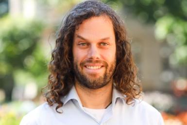 Nathaniel Geiger headshot. Curly-haired man wearing white button-up smiles