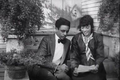 Screenshot of footage of two actors sitting on steps reading a letter together.