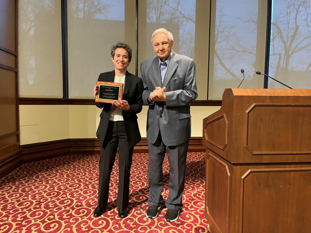 Amy Walter holds an award and stands next to Ted Carmines on the stage in Presidents Hall.