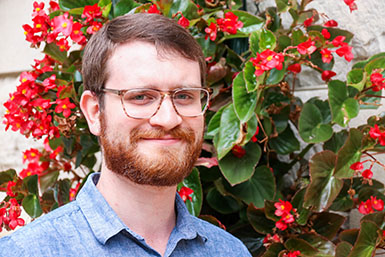 Headshot of Brennan with red flowers and leaves behind him. 