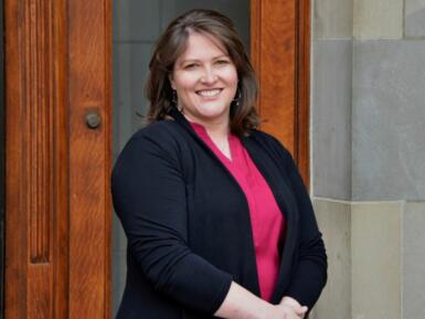 Headshot of Kelley French standing in front of a stone wall and wooden door.