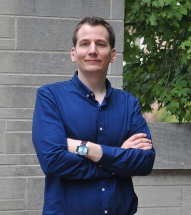 Headshot of Kyle Heatherly standing outside in front of a gray stone wall with his arms casually crossed.