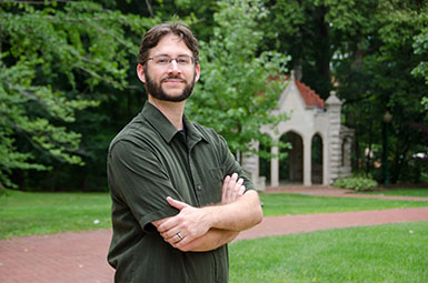 Will Emigh stands with his arms crossed in front of greenery.